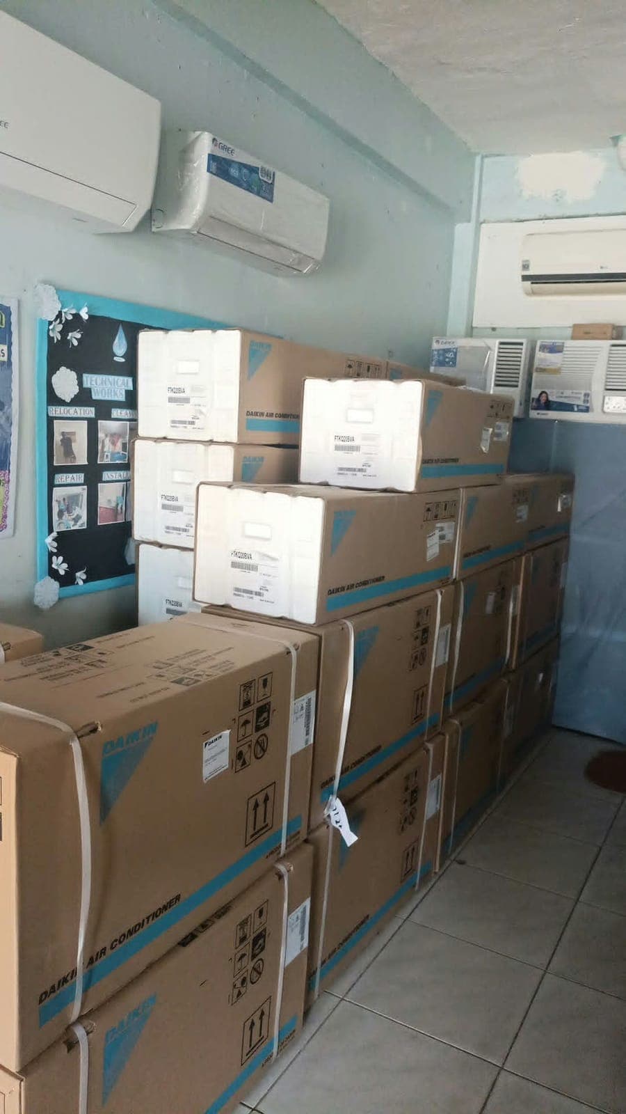Boxed new aircon units stacked in a shop, with display units on the wall